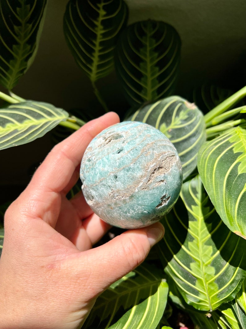May include: A green and white agate sphere with a swirling pattern. The sphere is smooth and polished.