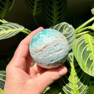 May include: A green and white agate sphere with swirling patterns. The sphere is smooth and polished.