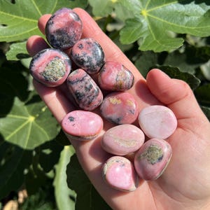 Peut inclure: Une collection de pierres roulées roses et noires. Les pierres sont lisses et polies, avec une variété de motifs et de textures.