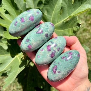 Könnte beinhalten: Vier glatte, ovalförmige Steine in Grün und Pink mit einem gesprenkelten Muster. Die Steine sind getrommelt und poliert.