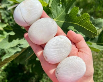 May include: Four white selenite palm stones with a striated pattern. The stones are smooth and polished.