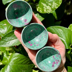 Könnte beinhalten: Drei grüne und rosafarbene Edelsteinschalen. Die Schalen sind rund und haben eine glatte, polierte Oberfläche.