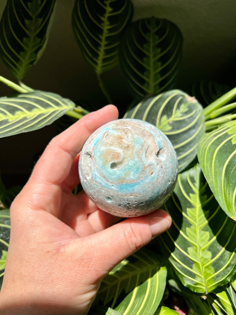 May include: A blue and white agate sphere with a swirling pattern. The sphere is smooth and polished.