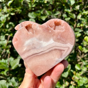 May include: A heart-shaped pink and white agate crystal with natural druzy formations. The crystal is polished and has a smooth, shiny surface.