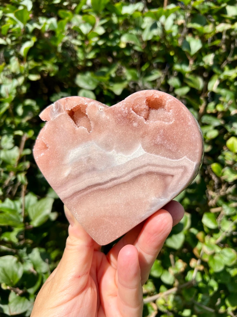 May include: A heart-shaped pink and white agate crystal with natural druzy formations. The crystal is polished and has a smooth, shiny surface.