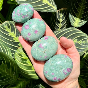 May include: Four green and pink tumbled stones with a speckled pattern. The stones are smooth and polished.