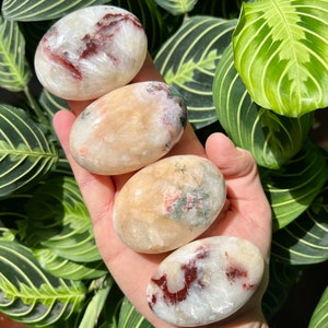 Op de afbeelding: Vier gladde, ovaalvormige gepolijste stenen met een witte basis en verschillende patronen in rood, roze en groen. De stenen zijn gestapeld, met de grootste steen onderaan en de kleinste steen bovenaan.