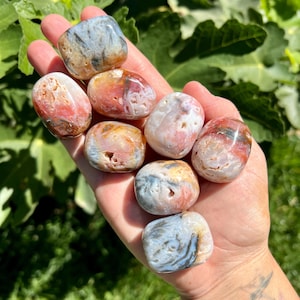 May include: A collection of eight tumbled stones with a variety of colours and patterns, including pink, white, grey, and brown. The stones are smooth and polished, and they have a natural, organic look.