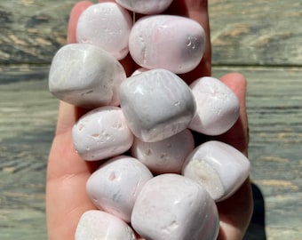 May include: A collection of tumbled pink selenite stones in various sizes and shapes. The stones are smooth and polished, with a soft, milky white colour.