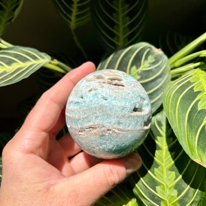 May include: A green and white agate sphere with a swirling pattern. The sphere is smooth and polished.