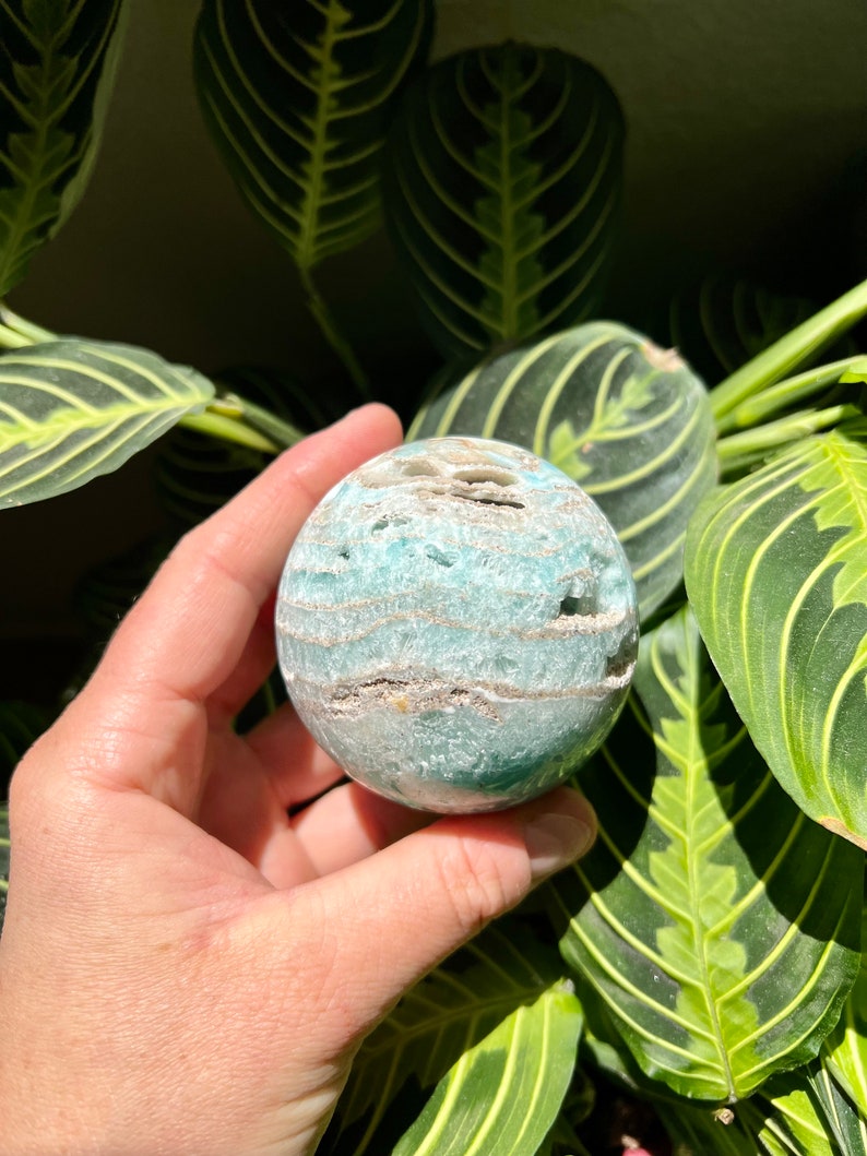 May include: A green and white agate sphere with a swirling pattern. The sphere is smooth and polished.