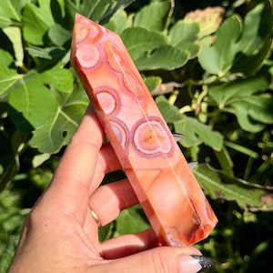 Peut inclure: Une tour en cristal polie de forme hexagonale présentant une palette de couleurs orange et corail vibrante avec des motifs circulaires et concentriques distincts sur toute la surface lisse et semi-translucide.