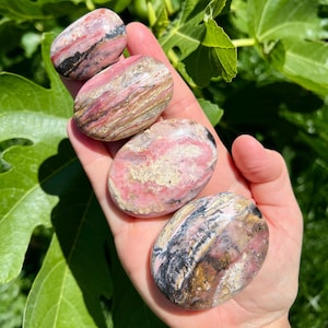 Puede incluir: Cuatro piedras lisas y pulidas de color rosa y negro con un patrón a rayas. Las piedras están apiladas, con la piedra más grande en la parte inferior y la más pequeña en la parte superior.