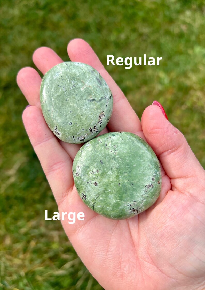 May include: Two green, oval-shaped stones are held in a hand. The top stone is labeled "Regular" and the bottom stone is labeled "Large". The stones have dark spots and a smooth texture. The background is blurred green.