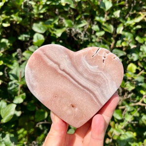 May include: A heart-shaped pink and white polished stone with natural striations and a smooth surface.