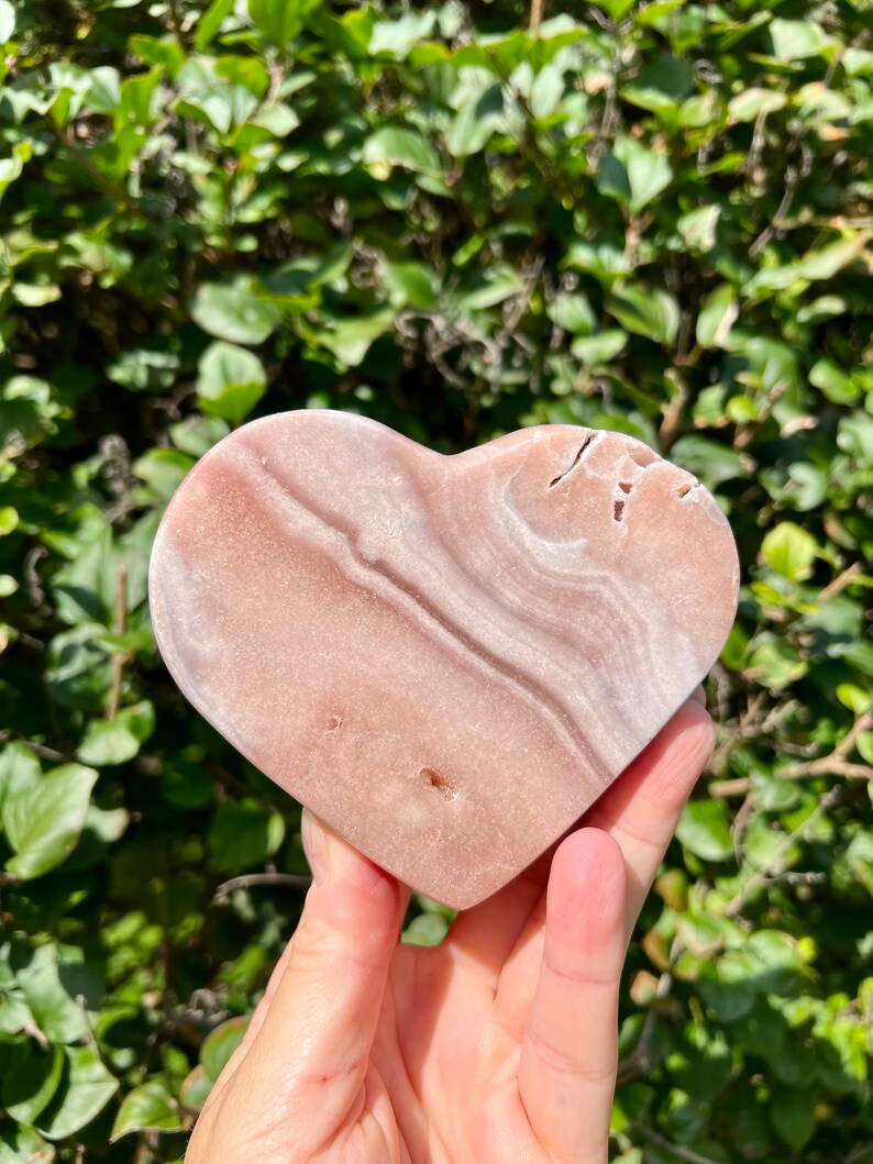 May include: A heart-shaped pink and white polished stone with natural striations and a smooth surface.