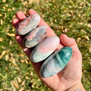 Può includere: Quattro pietre lisce di forma ovale con diversi motivi e colori. Le pietre sono un mix di rosa, verde, bianco e grigio.