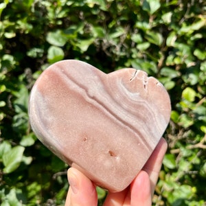 May include: A heart-shaped pink and white polished stone with natural striations and a smooth surface.