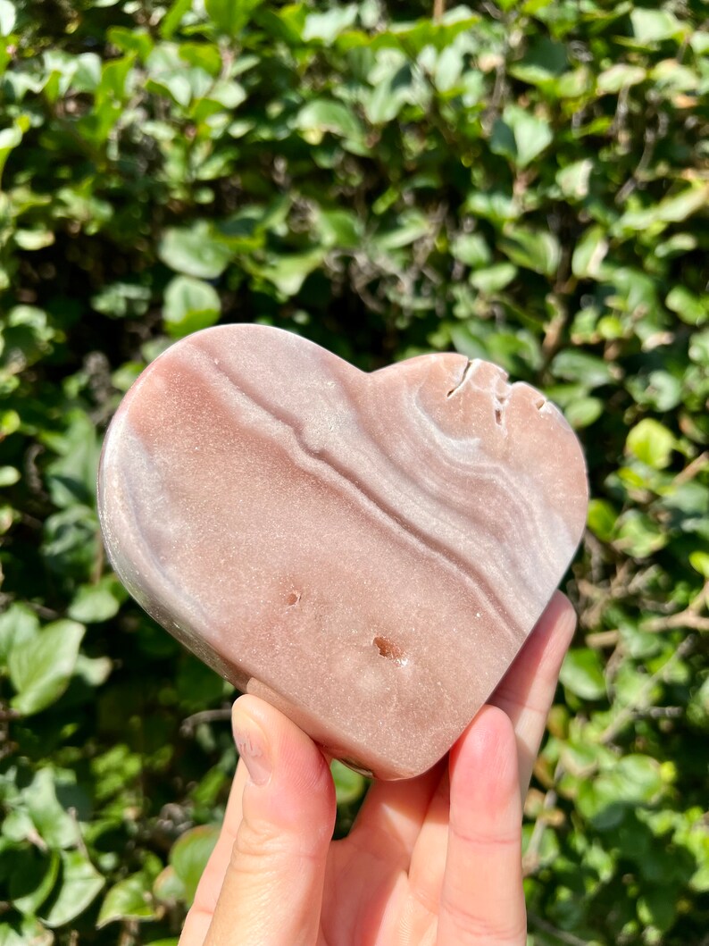 May include: A heart-shaped pink and white polished stone with natural striations and a smooth surface.