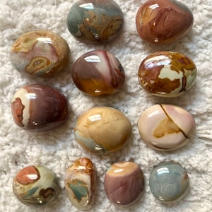 May include: A collection of 12 smooth, polished, multi-coloured, agate tumbled stones. The stones are various shades of brown, white, grey, and pink.