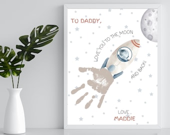 May include: A white framed print with a handprint in the shape of a rocket ship. The print says "To Daddy, Love you to the moon and back! Love, Maddie".