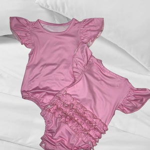 May include: Two pink baby onesies with ruffled sleeves and a ruffled bottom. The onesies are made of a soft, stretchy fabric.
