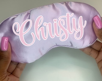 Puede incluir: Una máscara para dormir de satén lavanda con el nombre "Christy" bordado en rosa.