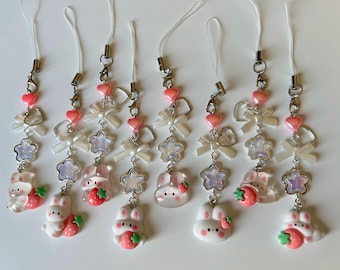May include: A collection of eight white and pink bunny charms with strawberry accents. Each charm features a white bow, pink heart beads, and a silver-tone clasp. The charms are connected to a white cord.