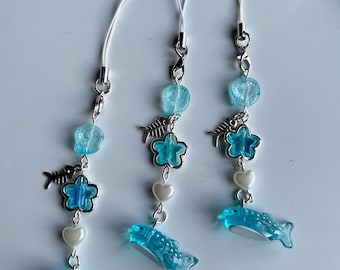 May include: Three blue and white phone charms with a dolphin, starfish, and heart design. Each charm has a silver fishbone charm and a blue and white bead.