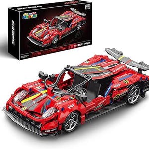 May include: A red toy race car with black and yellow accents, and a rear spoiler. The car is made of interlocking blocks and has the words "SPEED RACING" printed on the front. A black box with a picture of the car is in the background.