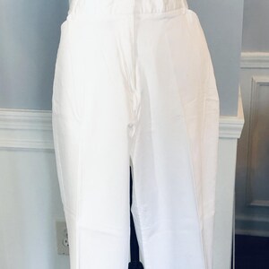 May include: White pants with a straight leg and a slightly flared hem. The pants are on a mannequin and are displayed against a white wall.