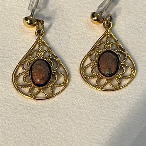 May include: A pair of gold filigree earrings with brown stone accents. The earrings are teardrop shaped and have a delicate floral design.
