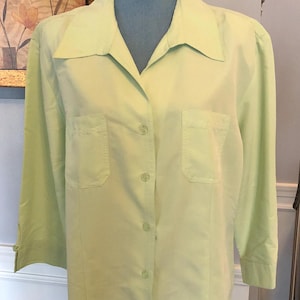 May include: A light green button-down shirt with long sleeves and two chest pockets. The shirt has a collared neckline and a button closure.