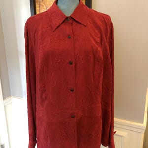 May include: A long-sleeved, red button-down shirt with a textured, floral pattern. The shirt has a collared neckline and button cuffs.