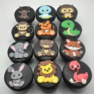 May include: A set of twelve circular black knobs, each featuring a raised, colorful cartoon animal figure. The animals include a deer, blue bird, owl, monkey, tiger, snake, elephant, bear, fox, rabbit, lion, and a pink flamingo.
