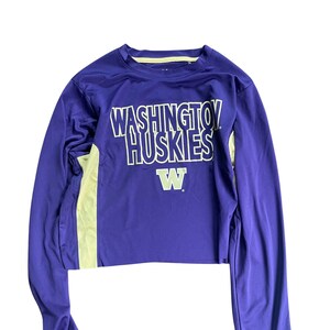 May include: Purple long-sleeve shirt with a yellow and white graphic that says "WASHINGTON HUSKIES" and a yellow "W" on the front.