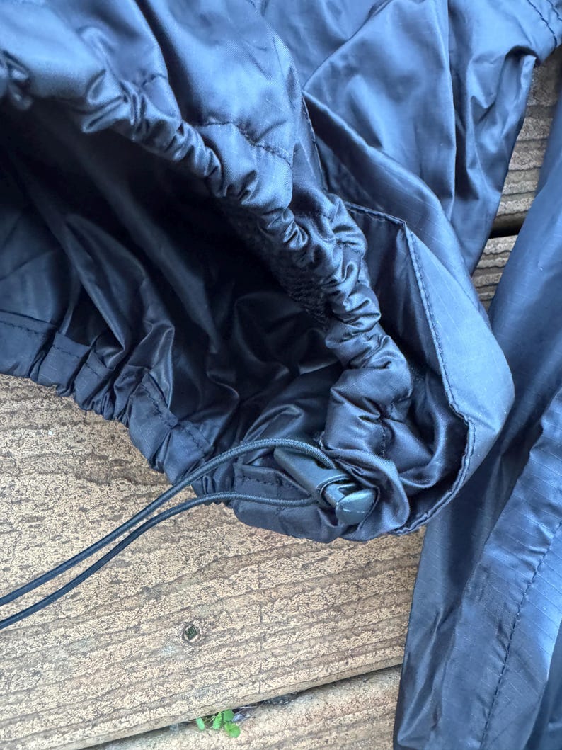 May include: Close-up of black nylon pants with an elastic waistband and drawstring. The pants have a quilted texture and a shiny finish. The drawstring is black and the pants appear to be new.