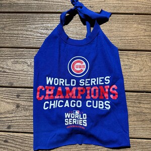 May include: A blue halter top featuring the Chicago Cubs logo and the words "World Series Champions." The text is in red and white. The top is made of a soft material and has a tie at the neck.