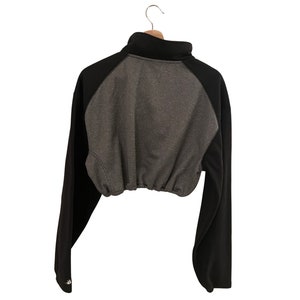 Op de afbeelding: Een zwart en grijs getailleerd sweatshirt met een hoge hals en lange mouwen. Het sweatshirt heeft een trekkoord aan de onderkant.
