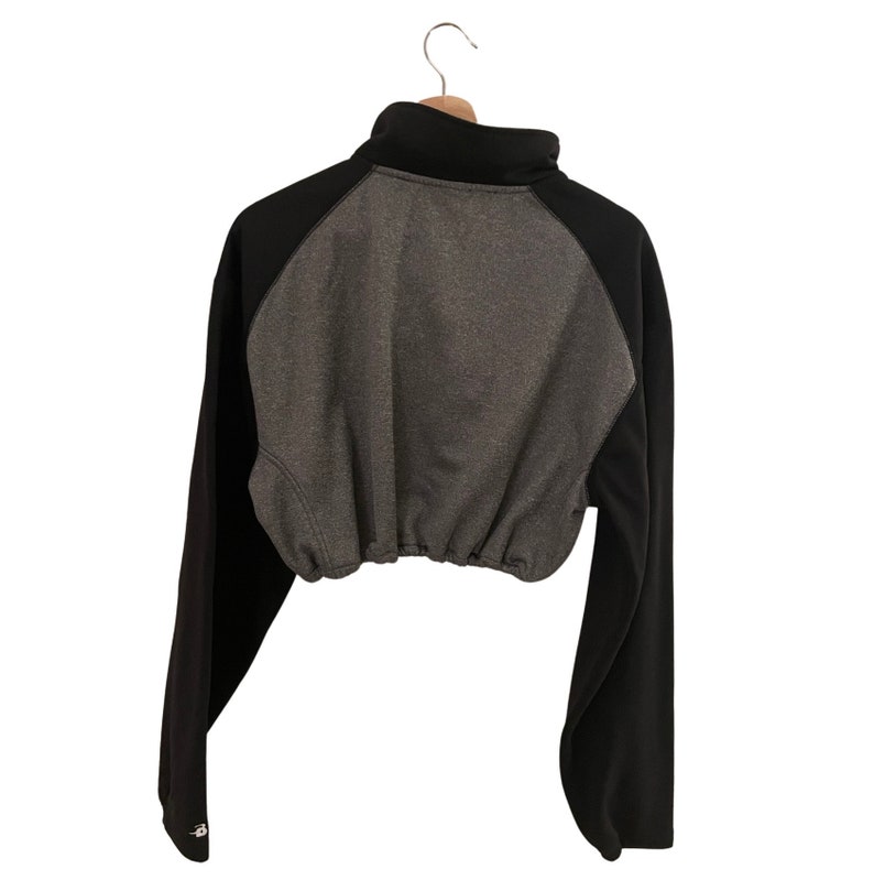 Op de afbeelding: Een zwart en grijs getailleerd sweatshirt met een hoge hals en lange mouwen. Het sweatshirt heeft een trekkoord aan de onderkant.