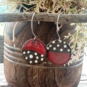 May include: A pair of circular drop earrings featuring a glossy finish with a split colour design of deep red and dark brown. The brown sections are decorated with small, raised white dots. The earrings hang from thin, silver-toned metal hooks.