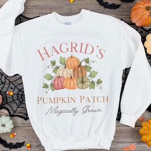May include: White sweatshirt featuring a graphic design of pumpkins and vines. The text "Hagrid's Pumpkin Patch Magically Grown" is printed on the sweatshirt.