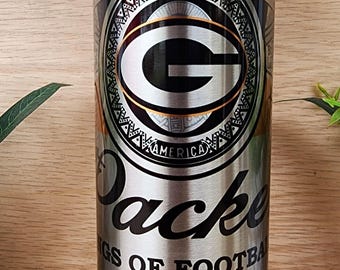 May include: A stainless steel tumbler with a gold rim and a Green Bay Packers logo. The tumbler has the text "Green Bay Packers" and "Kings of Football" on it. The tumbler also has the text "Est. 1919" and "America's Team Wisconsin U.S.A."