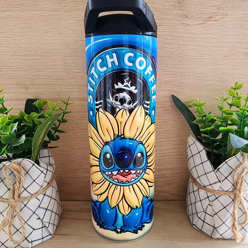 Puede incluir: Un vaso de acero inoxidable azul con tapa y asa negras. El vaso presenta un gr&aacute;fico de Stitch de Lilo & Stitch, con un girasol. El texto "Stitch Coffee" est&aacute; impreso en un c&iacute;rculo alrededor del gr&aacute;fico.
