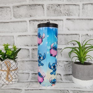 May include: A blue and pink stainless steel tumbler with a lid. The tumbler features a repeating pattern of a blue cartoon character with pink hearts.