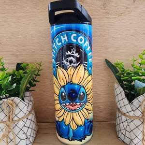 Puede incluir: Un vaso de acero inoxidable azul con tapa y asa negras. El vaso presenta una imagen de dibujos animados de Stitch de Lilo & Stitch con un girasol. El texto "Stitch Coffee" est&aacute; impreso en un c&iacute;rculo alrededor de la imagen.