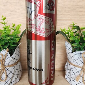 K&ouml;nnte beinhalten: Ein Edelstahlbecher mit einem rot-wei&szlig;-blauen Design. Der Becher zeigt einen Footballhelm und den Text "City" und "Genuine".