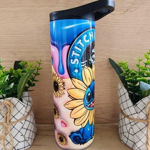 Puede incluir: Un vaso de acero inoxidable azul y rosa con una tapa negra. El vaso presenta un personaje de dibujos animados con un girasol y el texto "Stitch" en &eacute;l.