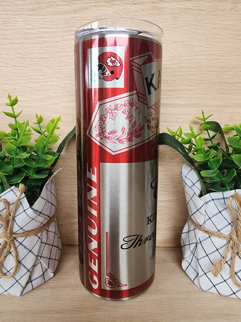 K&ouml;nnte beinhalten: Ein Edelstahlbecher mit einem roten und silbernen Design. Der Becher zeigt ein Logo der Kansas City Chiefs, ein Blumenmuster und die Worte "Genuine" und "The Most Rewarding."