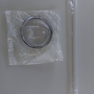 Puede incluir: Una tapa de pl&aacute;stico transparente para una taza de viaje con un sello de goma negro y una pajita de pl&aacute;stico transparente en un envoltorio de pl&aacute;stico.